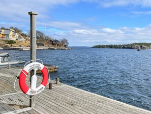 A wooden dock with a lifebuoy, a boat, and a distant shoreline with buildings. - 3 Person Holiday Home in Dalaro (Dalaro)