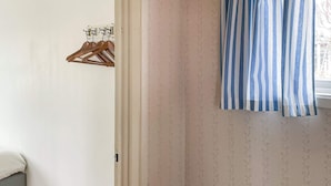 A room with a bed, a wooden hanger rack, and a window with striped curtains. - 3 Person Holiday Home in Dalaro (Dalaro)