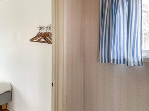A room with a bed, a wooden hanger rack, and a window with a striped curtain. - 3 Person Holiday Home in Dalaro (Dalaro)