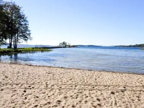 A sandy beach with footprints, a calm lake, and trees in the background. - 3 Person Holiday Home in Dalaro (Dalaro)