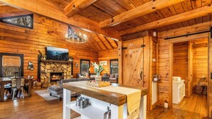 L’intérieur d’un chalet en bois comprend une cheminée en pierre, un coin repas et un salon avec un canapé et un téléviseur.