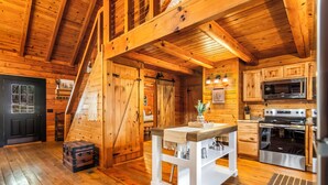 L’intérieur d’un chalet en bois comprend une cuisine, un coin repas et un escalier menant à un niveau supérieur.