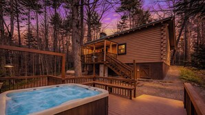 Une cabane en rondins avec un jacuzzi et une terrasse, entourée d’arbres.