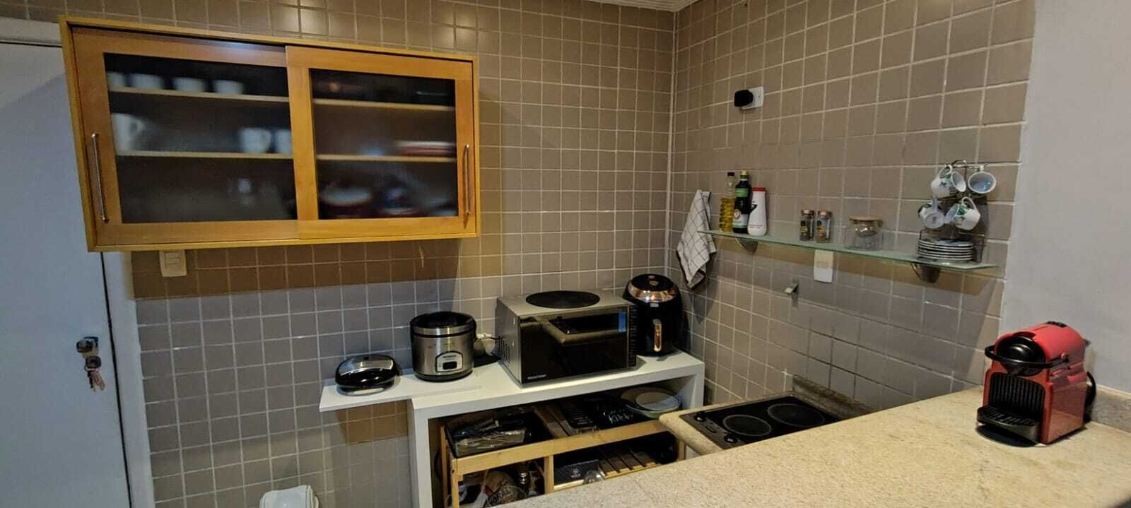 A compact kitchen with a microwave, toaster, and coffee maker on the countertop, a cabinet above, and a small shelf with kitchen items.