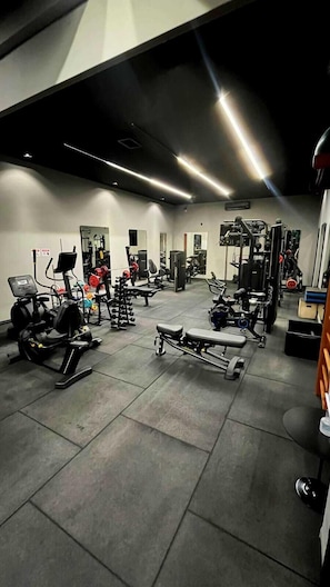 Uma academia com diversos equipamentos de exercício, incluindo esteiras, aparelhos de musculação e pesos livres.