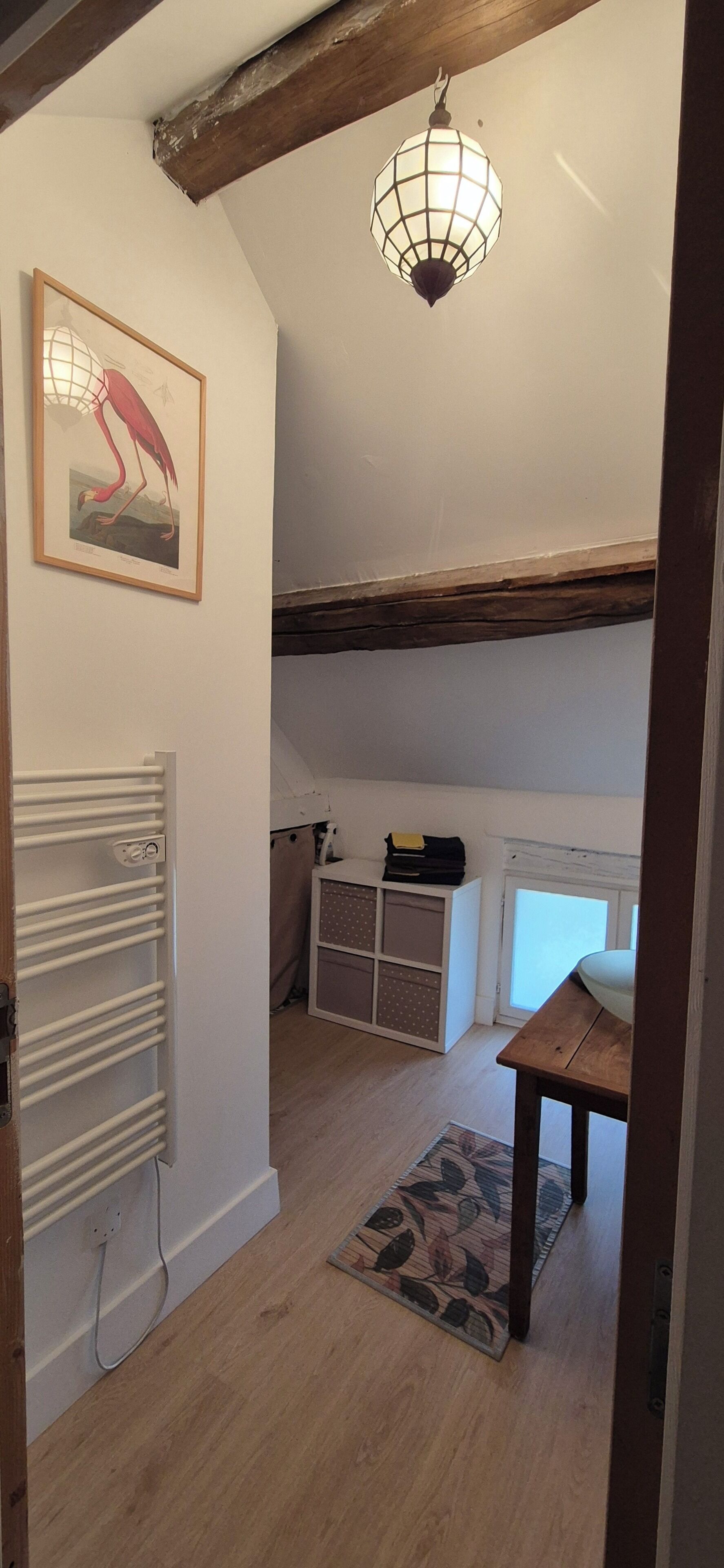 Et værelse med en radiator, et indrammet billede, en hængende lampe, en træbænk og et lille bord.