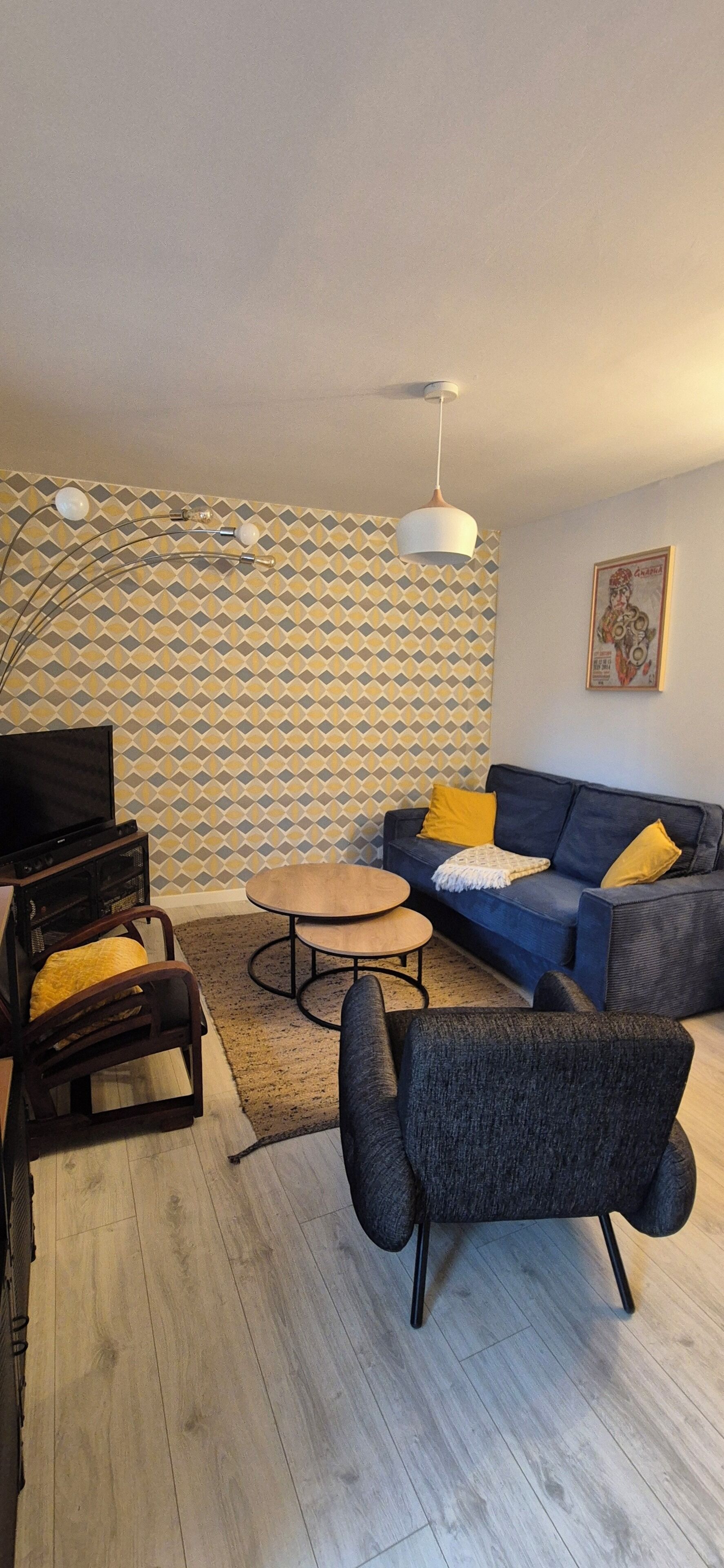 Una sala de estar con sofá, sillón, mesa de centro, televisor y papel tapiz estampado.
