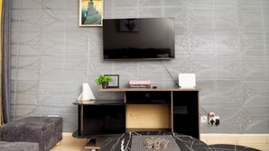 Una sala de estar moderna con un televisor de pantalla plana montado en la pared, un mueble de madera pequeño debajo y una pared con diseño gris.