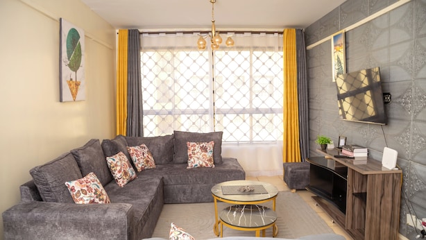 Una sala de estar con un sofá modular, una mesa de centro, un mueble para televisión y un ventanal con cortinas.