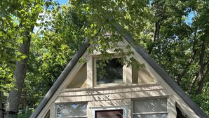A cabin with a red door, multiple windows, and a wooden deck. - Cozy 2-bedroom cottage in charming Pierson, Michigan! (Pierson)