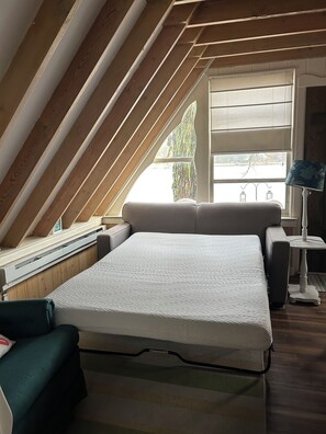 Une chambre à coucher aménagée dans un espace sous les toits, avec un plafond en pente, un lit, un banc, une table et une fenêtre donnant sur un beau paysage.