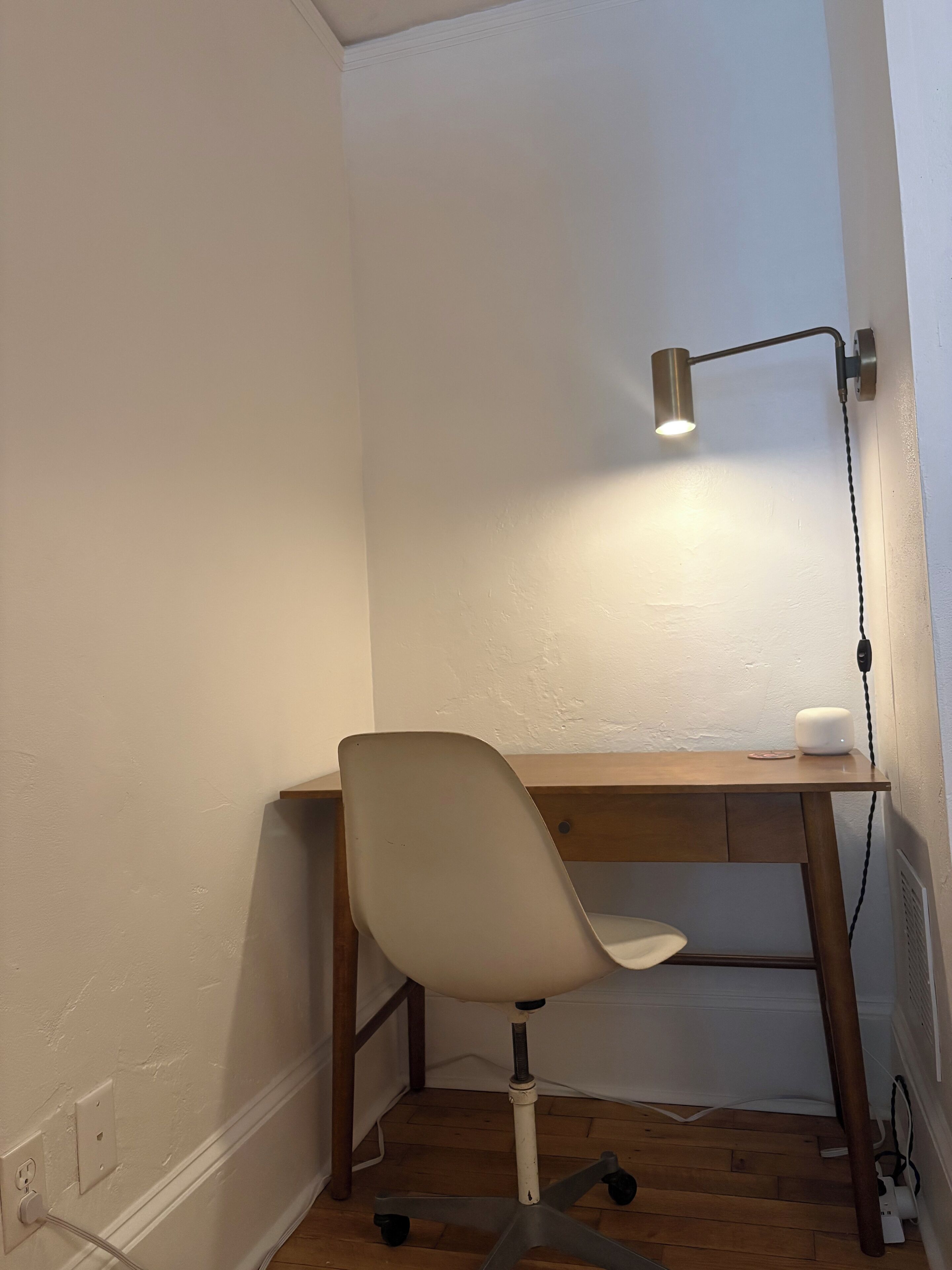 En arbetsplats i ett hörn, med ett skrivbord, en stol och en skrivbordslampa.