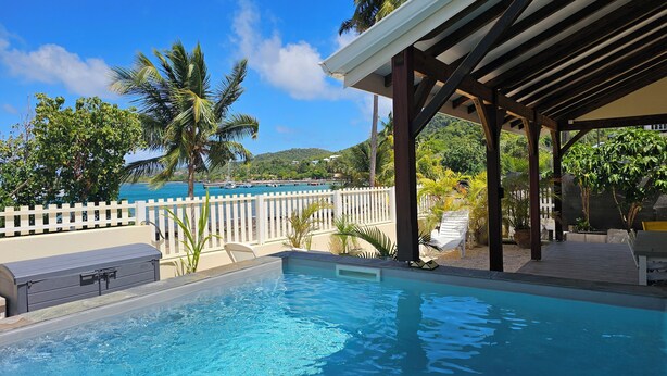 Une piscine avec vue sur la mer, un patio couvert et une clôture blanche.