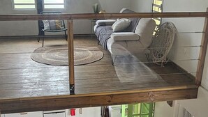 Une pièce de style loft avec un plafond haut, une table à manger en bois avec des chaises orange, un canapé et un petit coin cuisine.