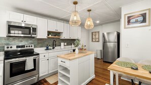 Una cocina moderna con armarios blancos, electrodomésticos de acero inoxidable, una isla de madera e iluminación colgante.