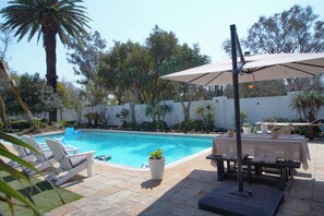 A swimming pool with lounge chairs and a table, surrounded by potted plants and trees. - French Bistro Studio - Home Near Sandton. High Wi-Fi Speed. Power&Water Backup (Sandton)