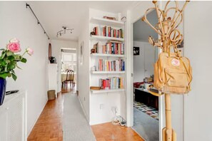 A hallway with a bookshelf, a radiator, a plant, and a backpack. - Serene garden 2-bed home with parking (London)