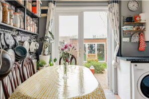 A kitchen with a dining table, a washing machine, and a view of the outside. - Serene garden 2-bed home with parking (London)