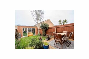 A backyard with a wooden deck, a dining table with chairs, and potted plants. - Serene garden 2-bed home with parking (London)