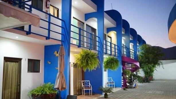 Un hôtel à la façade bleue et blanche, doté d’une terrasse avec des parasols et de plantes en pot.