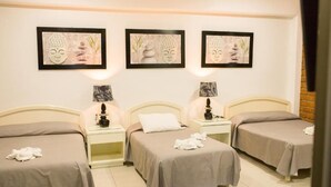 Une chambre d’hôtel avec trois lits simples, une table de chevet avec une lampe et des œuvres d’art murales représentant Bouddha.
