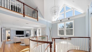 Un amplio salón con una escalera de madera, un candelabro y un gran ventanal.