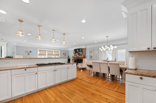 A modern kitchen with white cabinetry, a large island, and pendant lighting. - The Cove House: Upscale Coastal Living - Your Perfect Summer Escape! (Wareham)
