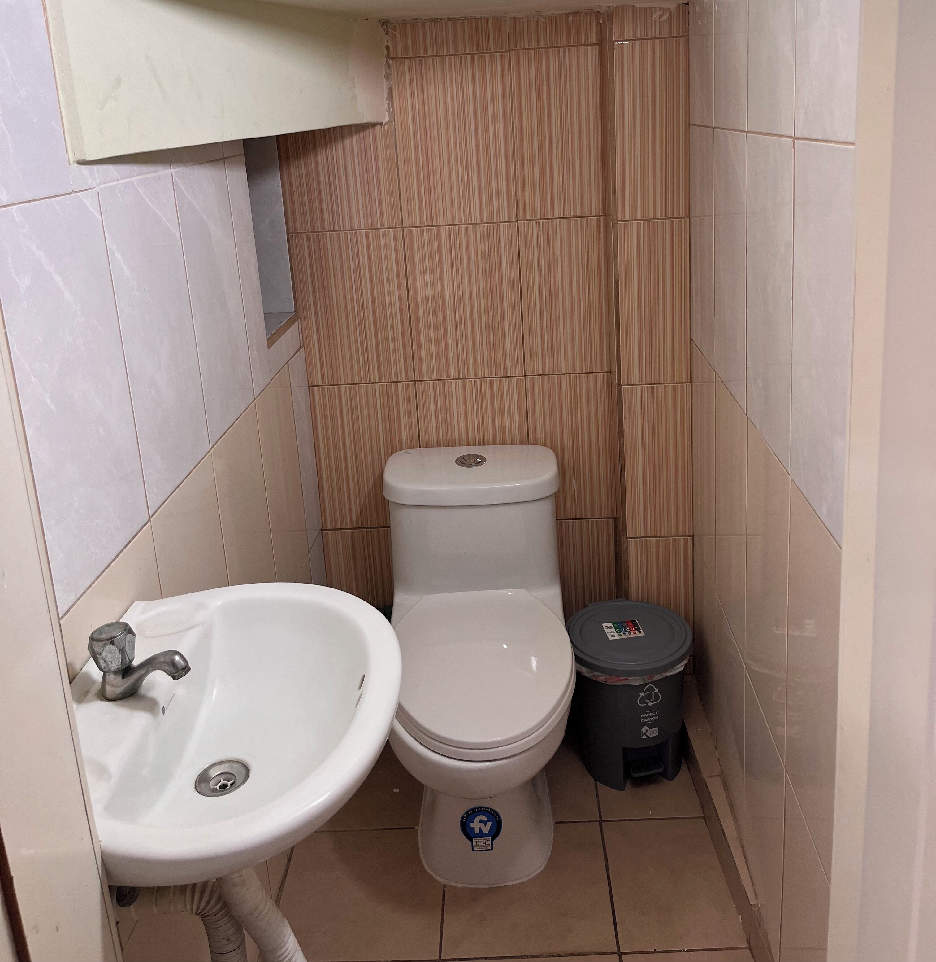 Un baño pequeño con lavamanos, inodoro y cubo de basura blancos.