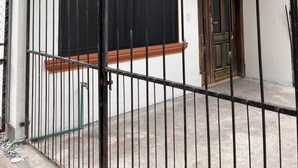Une entrée fermée par un portail mène à un bâtiment doté d’un toit recouvert de tuiles, d’une grande fenêtre et d’une porte.
