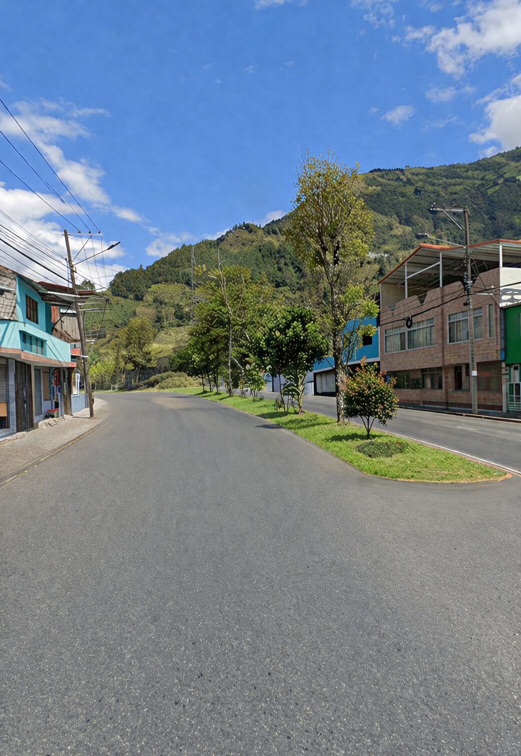 A quiet street with buildings on either side, a clear sky, and a hilly backdrop.