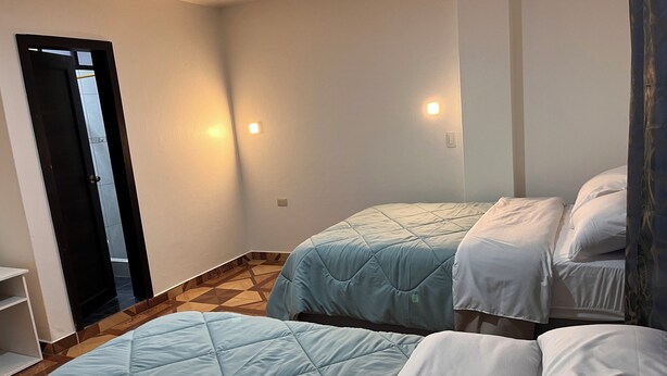 Une pièce avec deux lits, une porte et un luminaire fixé au mur.
