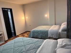 Une pièce avec deux lits, une porte et un luminaire fixé au mur.