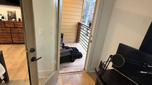 Une porte ouverte donnant sur un balcon équipé d’un barbecue, d’un plan de travail noir pour le barbecue et d’un plancher en bois.