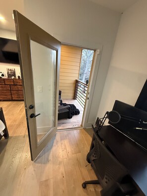 An open door leading to a balcony with a grill, a black grill station, and a wooden floor.