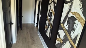Un couloir doté d’un plancher en bois, de murs noirs et de grandes peintures abstraites.