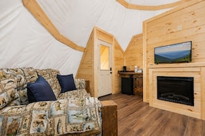 A cozy interior with a sofa, a fireplace, and a television mounted on the wall. - Flyin' Free Tepee | King Bed | Resort Access (Sevierville)