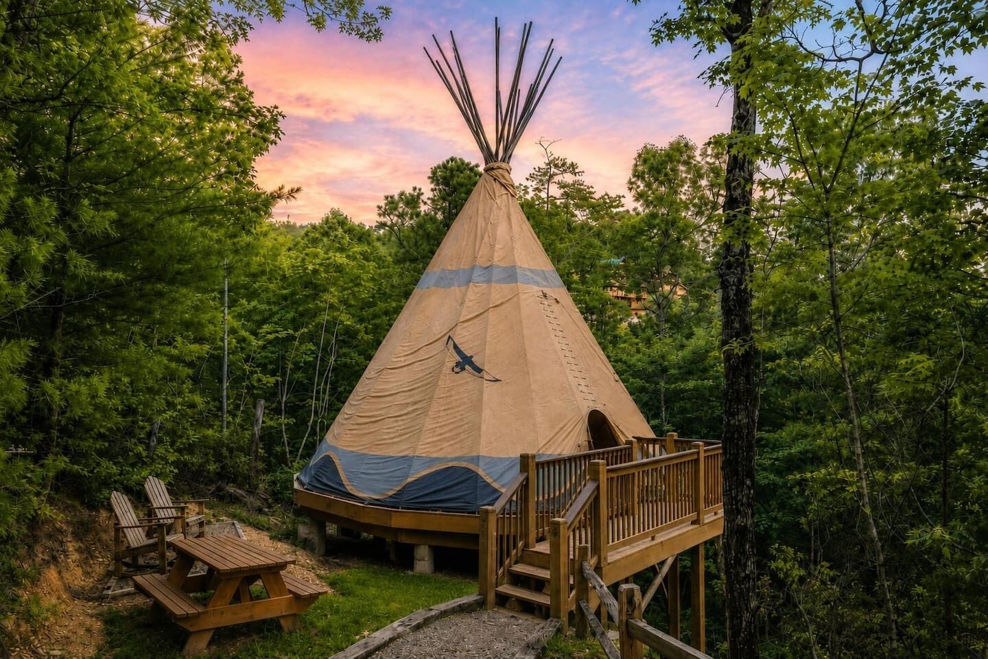 Una tienda de campaña tipi con una terraza de madera y mesas de picnic en un entorno boscoso.