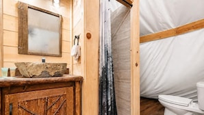 Une salle de bain rustique dans une cabane en bois, avec un lavabo, un miroir, un rideau de douche et des toilettes.