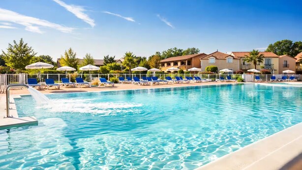 A swimming pool with clear blue water, surrounded by lounge chairs and umbrellas. - Appartement du Lac (Monflanquin)