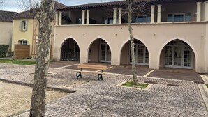 A building with a courtyard, arched doorways, and a bench. - Appartement du Lac (Monflanquin)