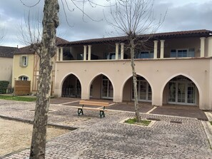 A building with a courtyard, arched doorways, and a bench. - Appartement du Lac (Monflanquin)
