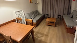 A modern living room with a wooden dining table, grey sofa, and a small wooden coffee table. - Appartement du Lac (Monflanquin)
