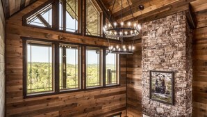 L’intérieur d’une cabane en rondins, avec de grandes fenêtres, une cheminée en pierre et un lustre.