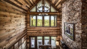 L’intérieur d’une cabane en rondins à plusieurs niveaux, avec un mur en pierre, de grandes fenêtres et un lustre.