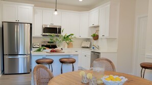 Una cocina moderna con armarios blancos, electrodomésticos de acero inoxidable y una mesa de comedor de madera con taburetes de bar.