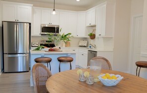 Una cocina moderna con armarios blancos, electrodomésticos de acero inoxidable y una mesa de comedor de madera con taburetes de bar.