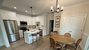 Una cocina moderna con armarios blancos, electrodomésticos de acero inoxidable, una isla central y un comedor con sillas de madera.