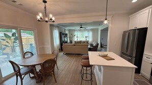 Una cocina amplia con una isla central, una mesa de comedor de madera y sillas, comunicada con una sala de estar que tiene un sofá y un ventilador de techo.