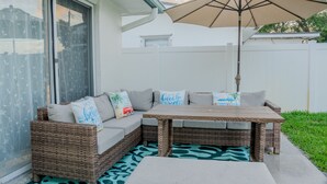 Un canapé d’angle en osier avec des coussins, une table en bois et un parasol beige.