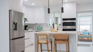 Une cuisine moderne équipée d’un réfrigérateur en acier inoxydable, d’un coin café et de deux tabourets de bar en bois.